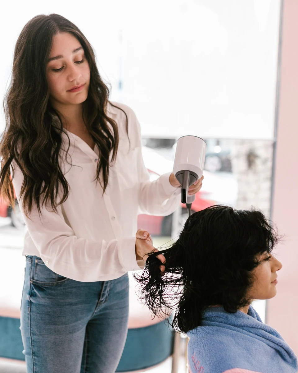 Eine Friseurin föhnt die Haare ihrer Kundin in einem hellen Salon.